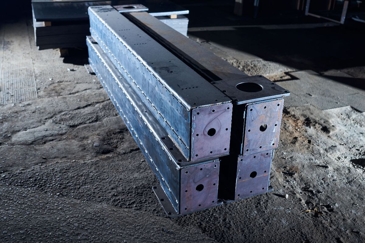 Heavy steel beams stacked on the ground inside a storage area