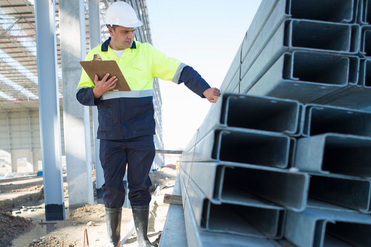 Construction worker inspecting stacked rectangular steel sections, showing steel materials suited for Philippine building conditions